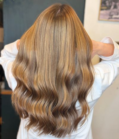Langt gyldent balayage-hår med bløde bølger, set bagfra